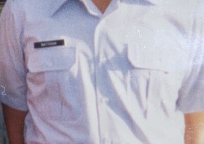 Hombre joven con uniforme militar y boina, de pie y sonriendo al aire libre, posiblemente promocionando una franquicia de ropa de marca.