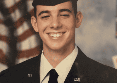 Un joven con uniforme de gala de la Fuerza Aérea de EE. UU. sonríe con orgullo frente a una bandera estadounidense.