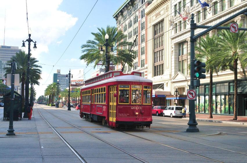 A red streetcar travels along a city street lined with palm trees and historic buildings on a sunny day.