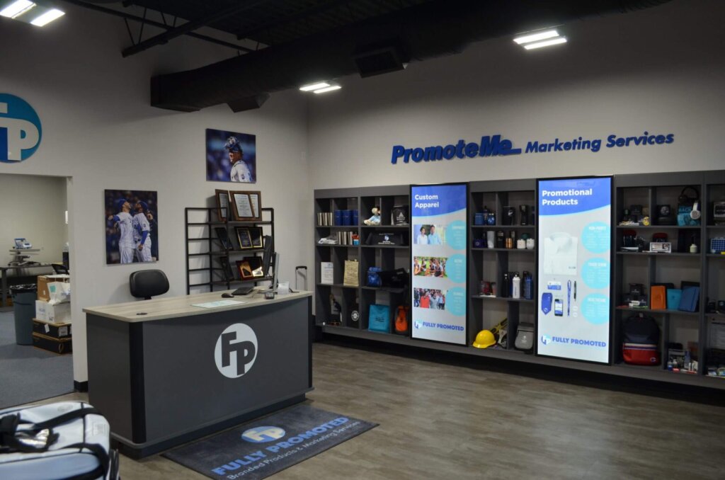 A marketing services office featuring a reception desk, product displays on shelves, and promotional posters on the walls. Illuminated signs and framed photos add to the decor.