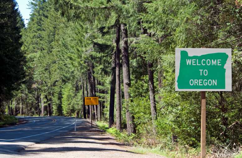 Welcome to Oregon" sign beside a winding road lined with lush green trees.