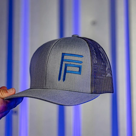 A gray and black trucker hat with a blue "FP" logo is held up against a blue-lit, metallic background.