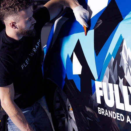 A person wearing a black "Flexwraps" shirt applies a colorful car wrap with a squeegee on a vehicle.