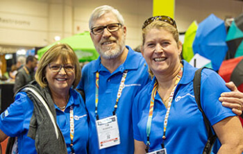 Three people in matching blue shirts at an event, smiling for the camera.